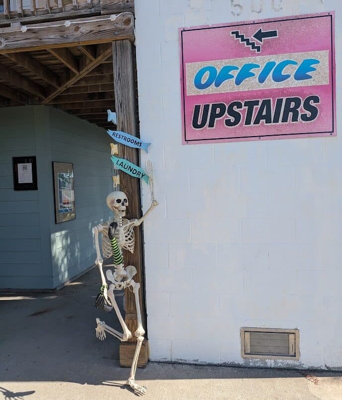 A skeleton pointing guests to the restrooms and laundry next to the Office Upstairs sign